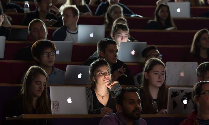The image shows a lecture hall full of students. They are all studying on their laptops.
