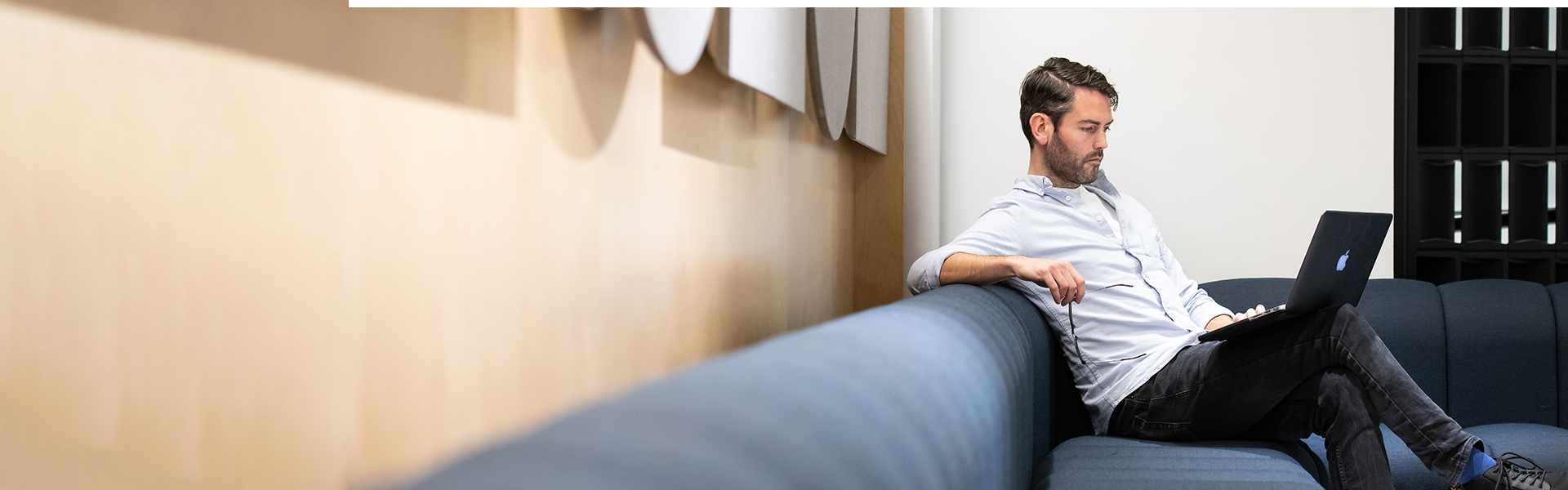 Man sitting on a blue sofa, looking at his laptop computer